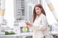 Beautiful young Asian professional working woman in a cream suit is using mobile phone smartphone to contact with partners while Royalty Free Stock Photo