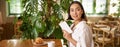 Beautiful young asian woman with a book in hands, sitting in cafe, drinking coffee and eating croissant, smiling Royalty Free Stock Photo