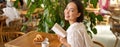 Beautiful young asian woman with a book in hands, sitting in cafe, drinking coffee and eating croissant, smiling Royalty Free Stock Photo