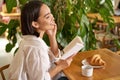 Beautiful young asian woman with a book in hands, sitting in cafe, drinking coffee and eating croissant, smiling Royalty Free Stock Photo