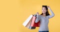 Beautiful young Asian woman carrying shopping bags looking surprised and happy isolated on yellow banner background with copy spac