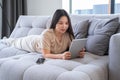 beautiful young asian woman in casual cozy clothes using tablet sitting on couch at modern apartment Royalty Free Stock Photo