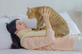 beautiful young asian woman cherishes a playful moment with her adorable cat on a cozy bed, bathed in bright morning light Royalty Free Stock Photo