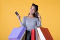 Beautiful young Asian woman with colourful shopping bags with smart phone and credit card isolated on yellow background Royalty Free Stock Photo