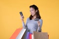 Beautiful young Asian woman with colourful shopping bags with smart phone and credit card isolated on yellow background Royalty Free Stock Photo