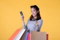 Beautiful young Asian woman with colourful shopping bags with smart phone and credit card isolated on yellow background Royalty Free Stock Photo