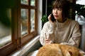 A woman talking on the phone with someone while her cat is sleeping on a table