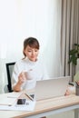 Beautiful young Asian woman drinking tea or coffee while working with laptop at home Royalty Free Stock Photo