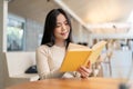 A beautiful young Asian woman enjoys reading a book while relaxing in a coffee shop Royalty Free Stock Photo