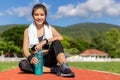Beautiful young Asian woman in fitness outfit sitting on running track and smiling at camera at an outdoor sport field on a bright Royalty Free Stock Photo