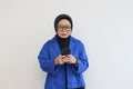 Beautiful young Asian woman in glasses, hijab and wearing a blue blazer looking at her mobile phone with a sad face Royalty Free Stock Photo