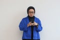 beautiful young asian woman in glasses, hijab and wearing blue blazer looking at her mobile phone with sullen face Royalty Free Stock Photo