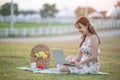 Beautiful young Asian woman having picnic on sunny spring day in park, happy reading things on internet, having cup of coffee, and Royalty Free Stock Photo