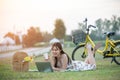 Beautiful young Asian woman having picnic on sunny spring day in park, happy reading things on internet, having cup of coffee, Royalty Free Stock Photo