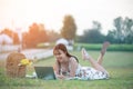 Beautiful young Asian woman having picnic on sunny spring day in park, happy reading things on internet, having cup of coffee, Royalty Free Stock Photo