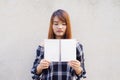 Beautiful young asian woman hiding behind a blank mock up book on concrete wall background. Vintage effect style pictures Royalty Free Stock Photo