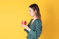 Beautiful young Asian woman hold coffee feel warm with hot red cup stand on yellow background in studio, portrait attractive lady