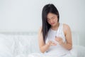 Beautiful young asian woman holding drug and glass of water while ill sitting on bed in the bedroom at home. Royalty Free Stock Photo