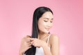 Beautiful young Asian woman holding her healthy hair and combing her hair on pink background Royalty Free Stock Photo