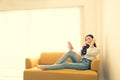 Beautiful young Asian woman listening music with headphones using a tablet on sofa in the room, Royalty Free Stock Photo