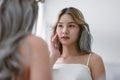 Beautiful young asian woman looking at mirror touching her skin enjoying treatment for skin. Korean or Japanese influencer girl