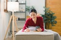 A beautiful young Asian woman is lying on a sofa, writing in her diary with a pen and notebook in her hands. She is a Royalty Free Stock Photo