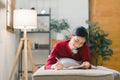 A beautiful young Asian woman is lying on a sofa, writing in her diary with a pen and notebook in her hands. She is a Royalty Free Stock Photo