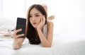 Beautiful young Asian woman making selfie using a smartphone and smiling while lying on bed. People addiction to new technology Royalty Free Stock Photo
