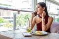 Beautiful young asian woman in red dress sitting in the restaurant looking out the window calling with smartphone . happy elegant