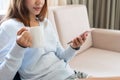 Beautiful young Asian woman relaxing on sofa at home and using smartphone while drinking coffee. Closeup Royalty Free Stock Photo