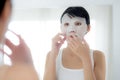 Beautiful young asian woman with sheet facial mask and looking mirror at home, beauty girl applying cosmetic and makeup. Royalty Free Stock Photo