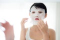 Beautiful young asian woman with sheet facial mask and looking mirror at home, beauty girl applying cosmetic and makeup. Royalty Free Stock Photo