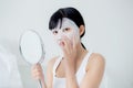 Beautiful young asian woman with sheet facial mask and looking mirror at home, beauty girl applying cosmetic and makeup. Royalty Free Stock Photo