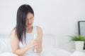 Beautiful young asian woman sitting on bed holding water of glass and drinking in the morning in bedroom at home. Royalty Free Stock Photo