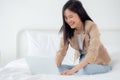 Beautiful young asian woman sitting on bed using laptop computer working from home in the bedroom. Royalty Free Stock Photo