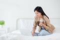 Beautiful young asian woman sitting on bed using laptop computer working from home and holding coffee cup. Royalty Free Stock Photo