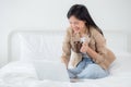 Beautiful young asian woman sitting on bed using laptop computer working from home and holding coffee cup in the bedroom. Royalty Free Stock Photo