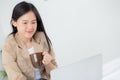 Beautiful young asian woman sitting on bed using laptop computer working from home and holding coffee cup. Royalty Free Stock Photo