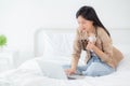 Beautiful young asian woman sitting on bed using laptop computer working from home and holding coffee cup. Royalty Free Stock Photo