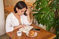 Beautiful young asian woman sitting in cafe with a book, eating croissant and reading, drinking cup of coffee Royalty Free Stock Photo
