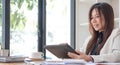 Beautiful young asian woman sitting at coffee shop using laptop. Happy young businesswoman sitting at table in cafe with tab top Royalty Free Stock Photo