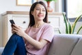 Beautiful young asian woman sitting on sofa using her phone and looking out the window Royalty Free Stock Photo