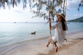 A beautiful young woman sitting on swing at the beach with a dog playing water in the sea Royalty Free Stock Photo