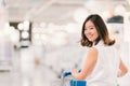 Beautiful young Asian woman smiling, with shopping cart, shopping center or department store scene, blur bokeh background Royalty Free Stock Photo