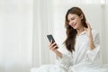 Beautiful young asian woman smiling sitting relax on the bed in the morning, girl using mobile smart phone talking enjoy Royalty Free Stock Photo