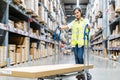 Beautiful young Asian woman staff worker pushing trolley or picking cart  to arrange things in warehouse store Royalty Free Stock Photo