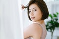 Beautiful young Asian woman standing near a window white curtains and turning to look and smile at camera. Pretty young girl Royalty Free Stock Photo