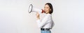 Beautiful young asian woman talking in megaphone, screams in speakerphone and smiling, making announcement, shout out Royalty Free Stock Photo