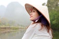 Beautiful young Asian woman in the traditional cone hat with misty mountains on the background