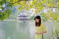 Beautiful young Asian woman in traditional yellow dress standing on the lake shore with small pagoda